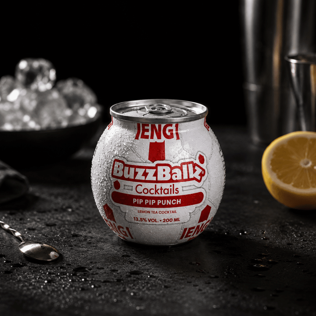 Condensation-covered BuzzBallz Pip Pip Punch Lemon Tea cocktail can on a dark counter with ice in the background on the left and a lemon half on the right.